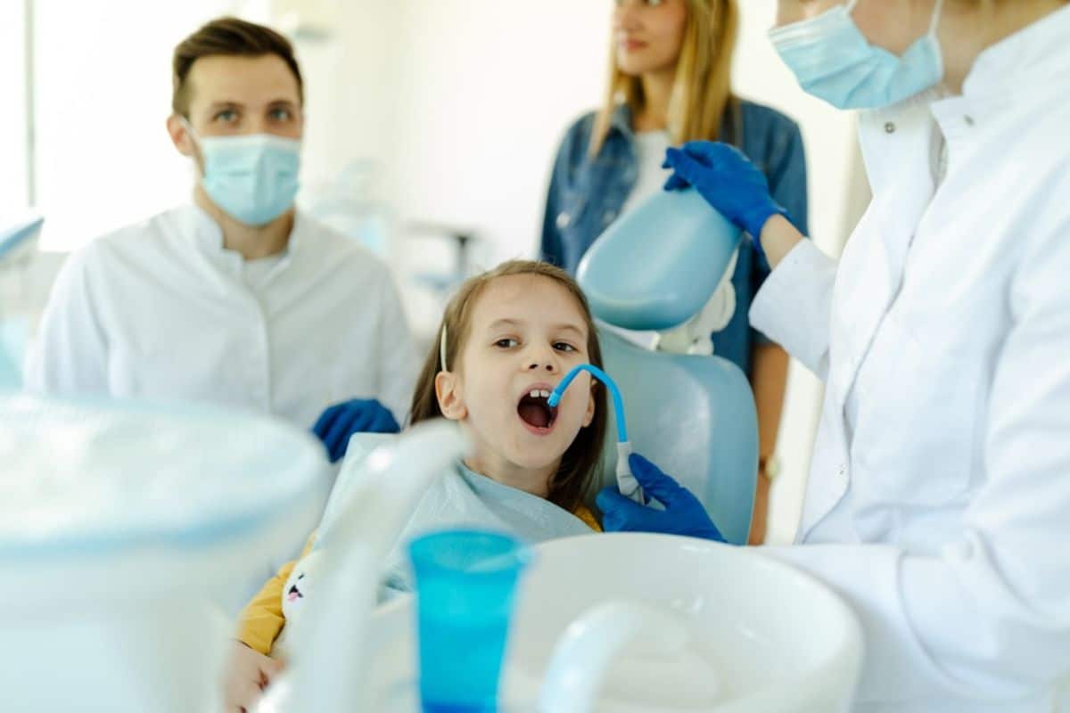Child in dental chair surrounded by dentist and assistants in professional dental office setting.